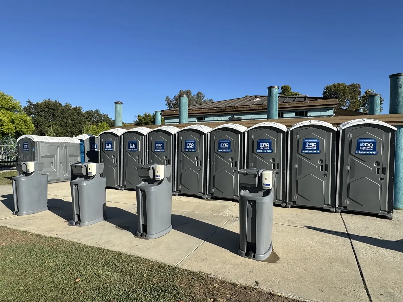 Hand-wash stations lined up in front of a row of portable restrooms at a San Jose park
