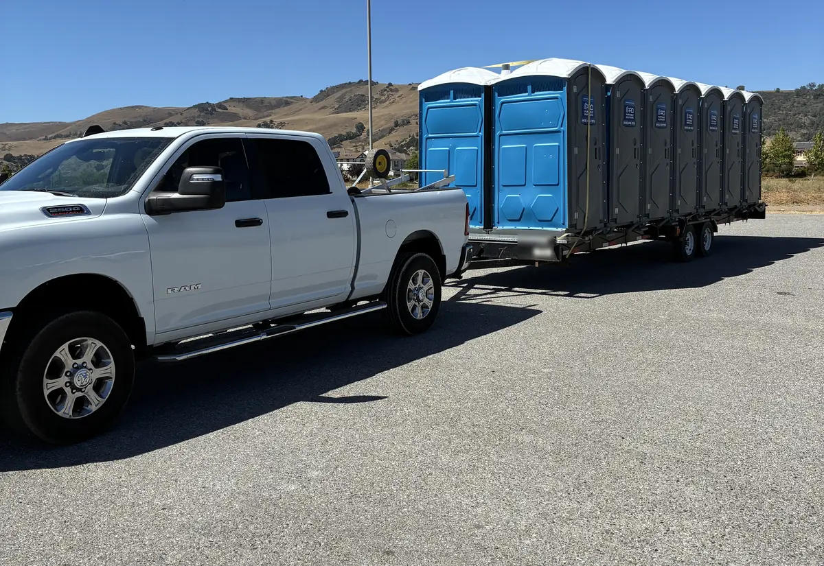 A pickup towing a trailer loaded with Pro Portable Restrooms units before the San Jose park event