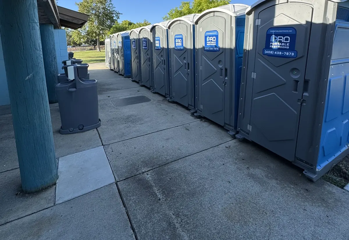 A row of Pro Portable Restrooms units along the walkway beside a park building in San Jose