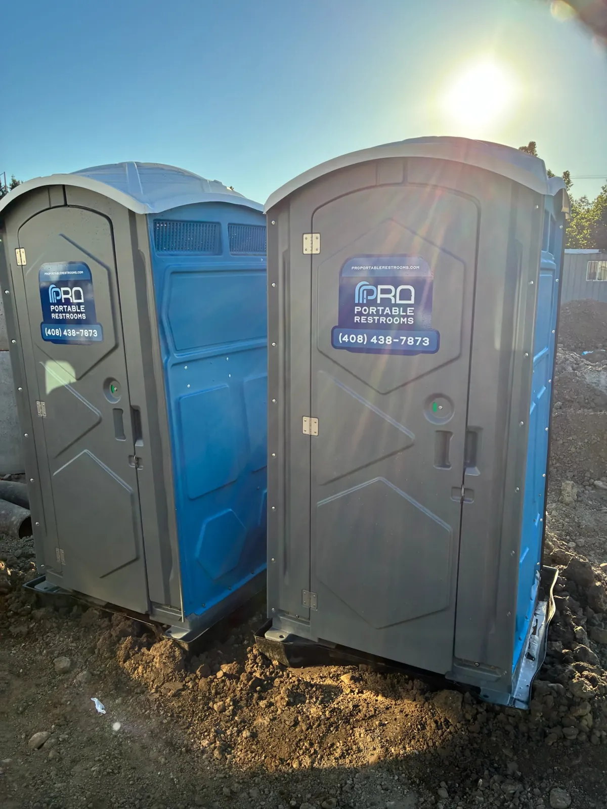Two Pro Portable Restrooms units on site with the sun flaring behind them